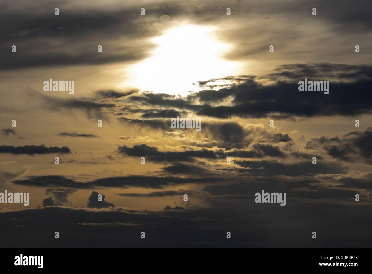 Ciel de coucher de soleil spectaculaire avec un soleil intensément brillant avant de se coucher. Les nuages sombres et orageux flottent à travers l'horizon vif, créant un puissant et captivant Banque D'Images