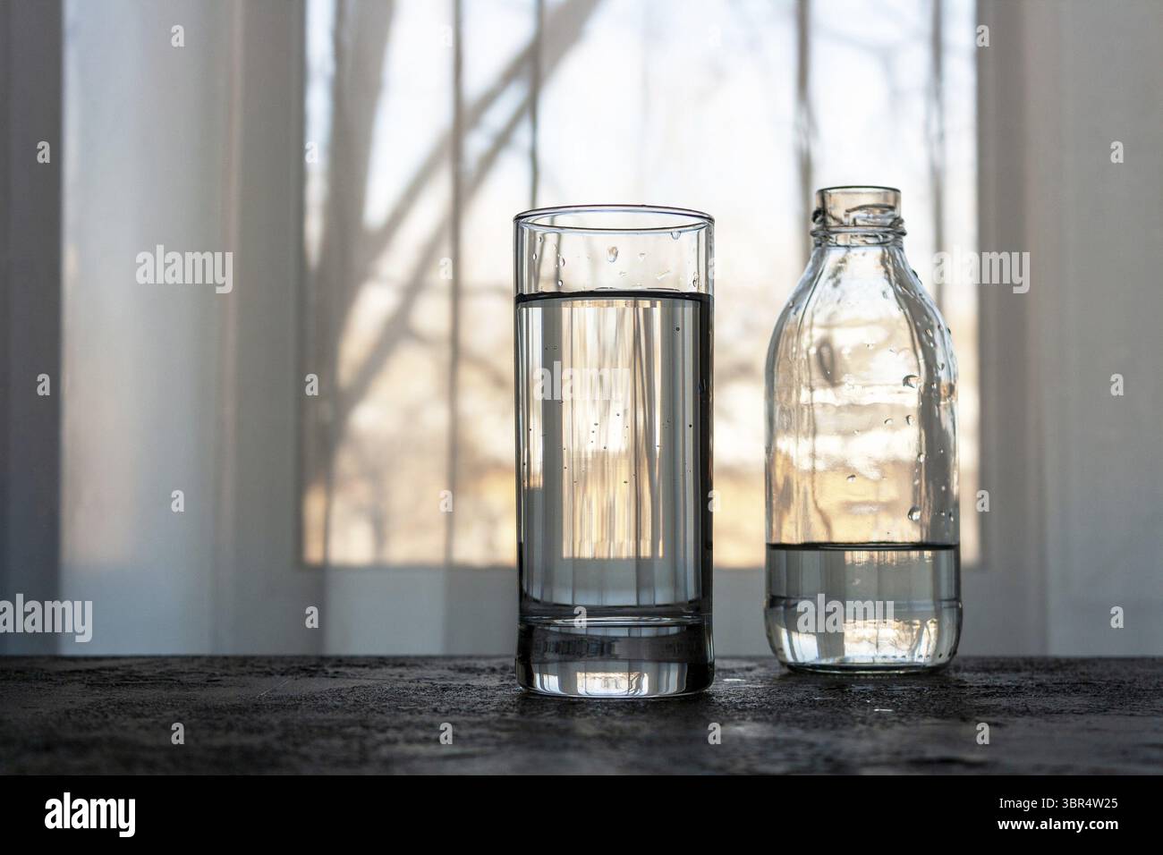 Un verre d'eau et une bouteille sont sur la table près de la fenêtre Banque D'Images