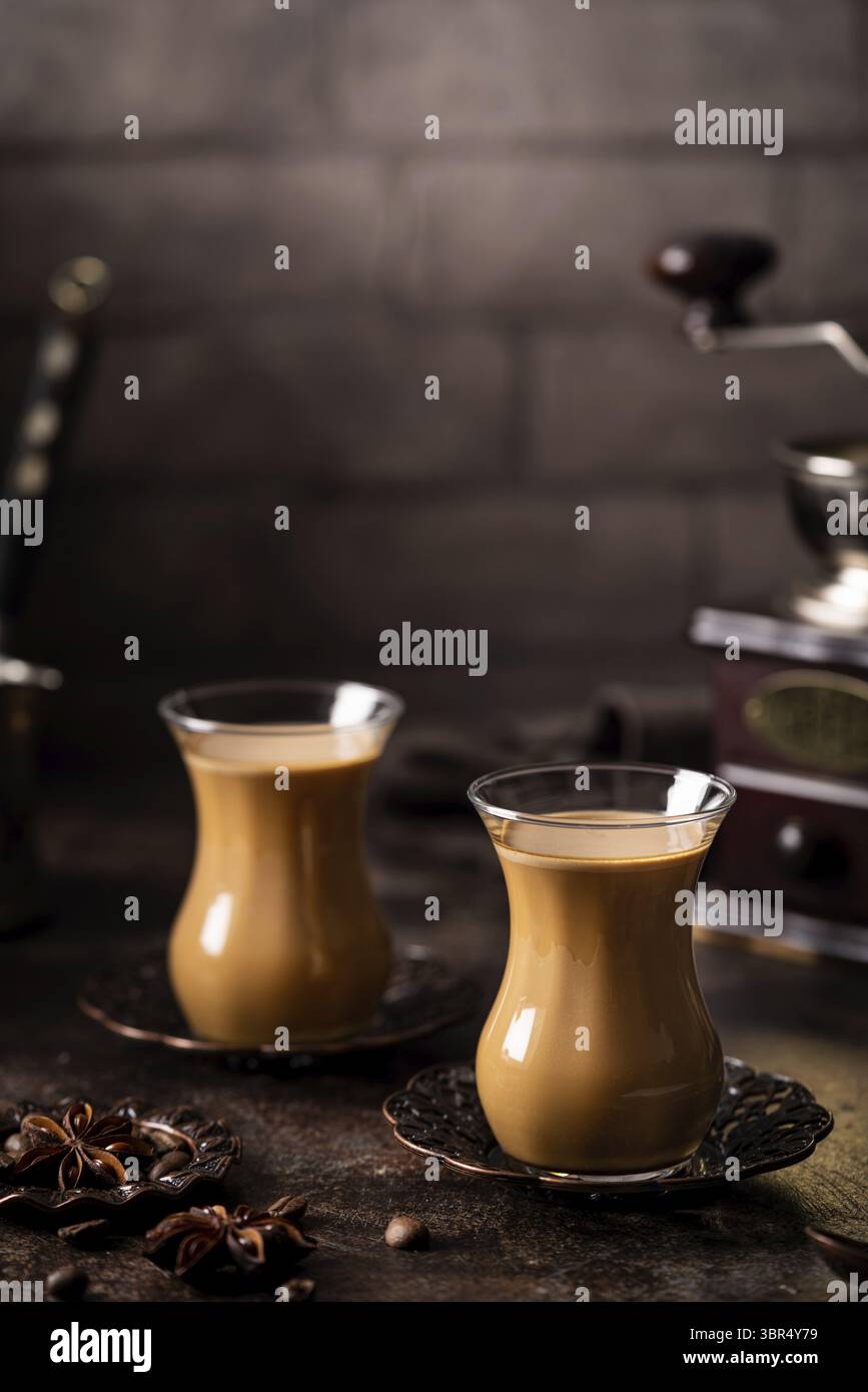 Thé ou café avec du lait et des épices en verre Armudu avec des grains de café et du sucre sur fond sombre Banque D'Images