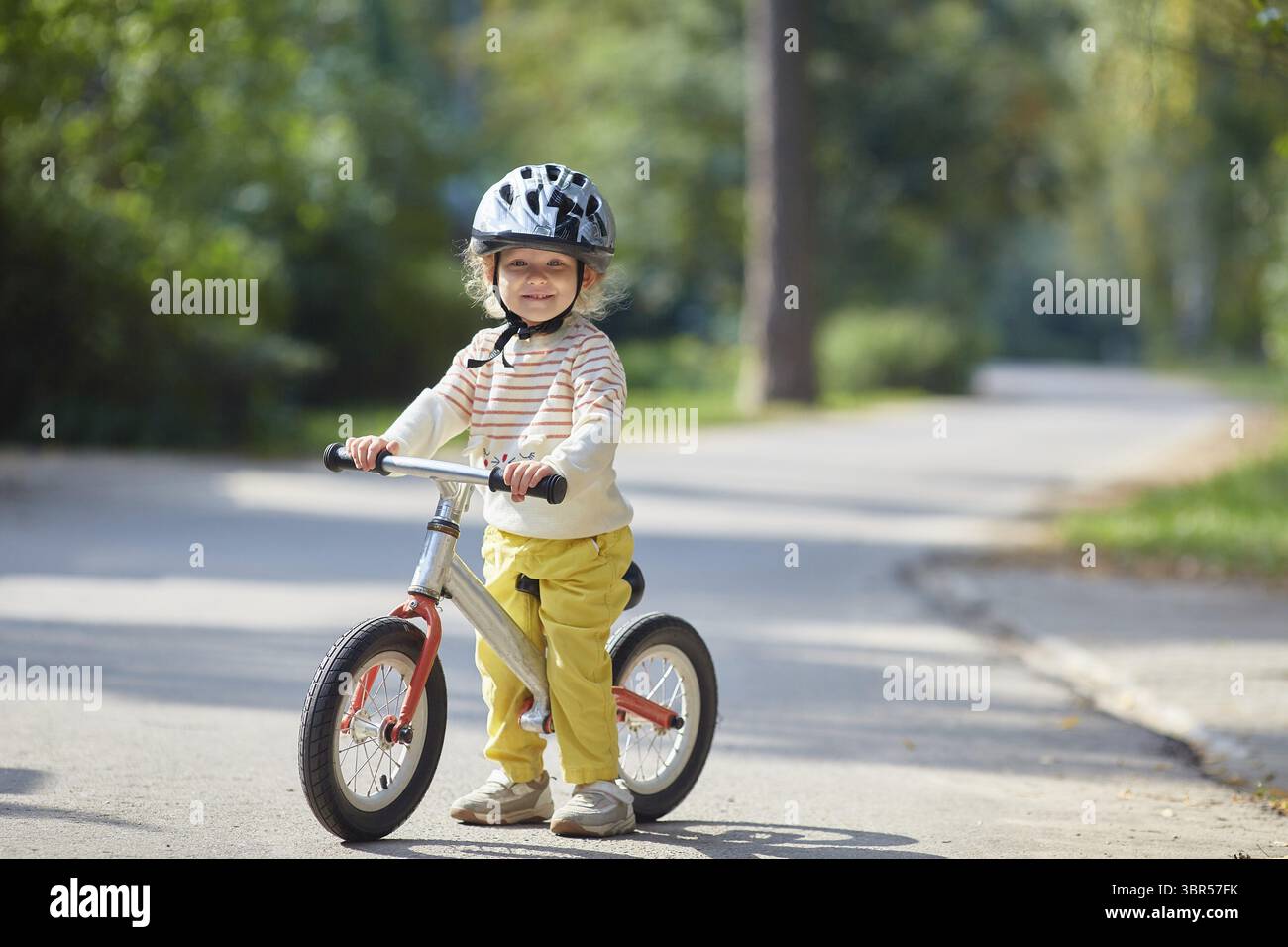 Zufriedenes Kind auf einem Balance-Bike mit einem Helm. Un einem sonnigen Sommertag Banque D'Images