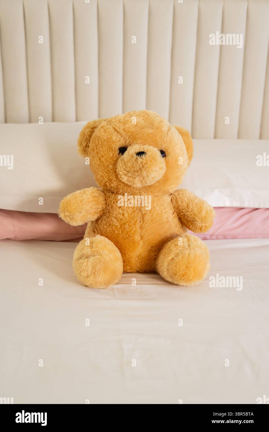 Ours en peluche repose sur des draps de lit blancs à côté d'un oreiller rose pâle, tête de lit touffetée crème Banque D'Images