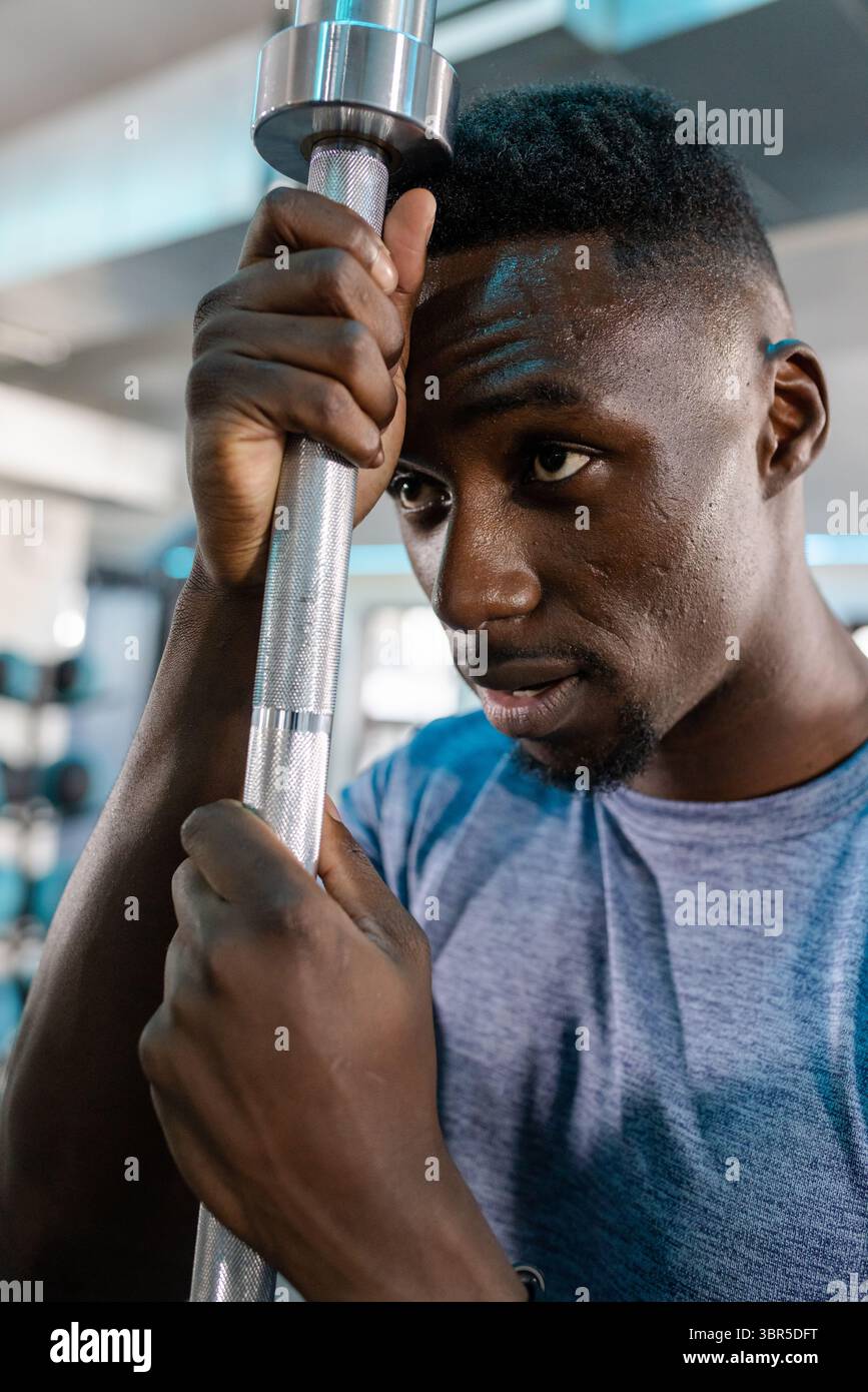 Homme afro-américain en tee bleu saisissant la barre métallique moletée tout en travaillant sur la machine de musculation Banque D'Images
