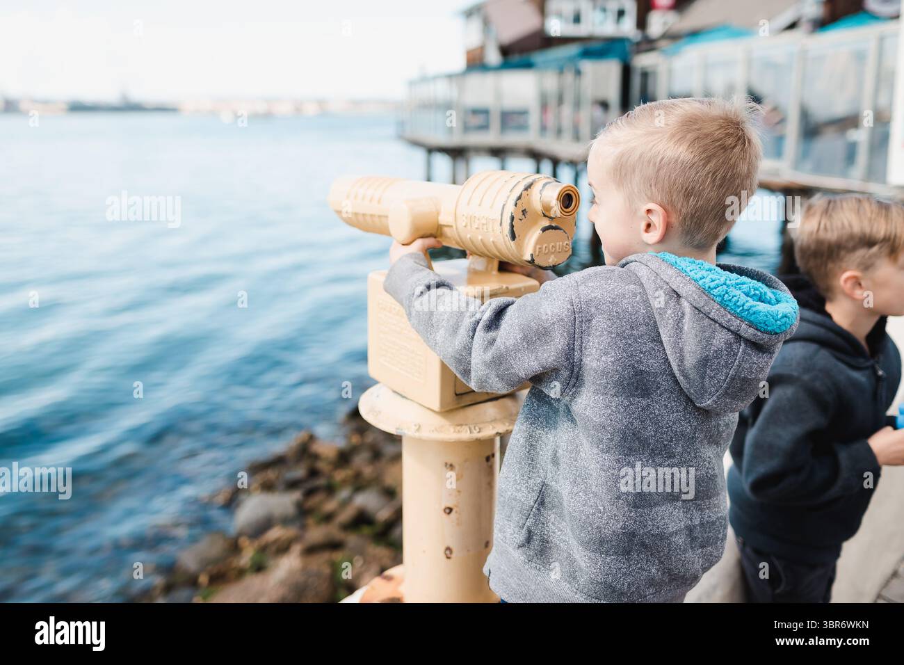 Enfant explorant la vue sur l'océan avec télescope de la jetée Banque D'Images