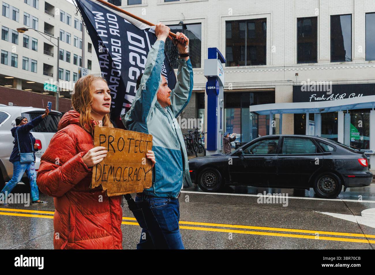 Un couple marche ensemble dans une marche de protestation sous la pluie tenant des panneaux Banque D'Images