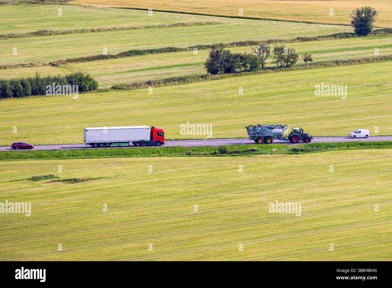 Vue aérienne à un tracteur sur une route de campagne avec des voitures et camion dans un paysage cultivé en été Banque D'Images