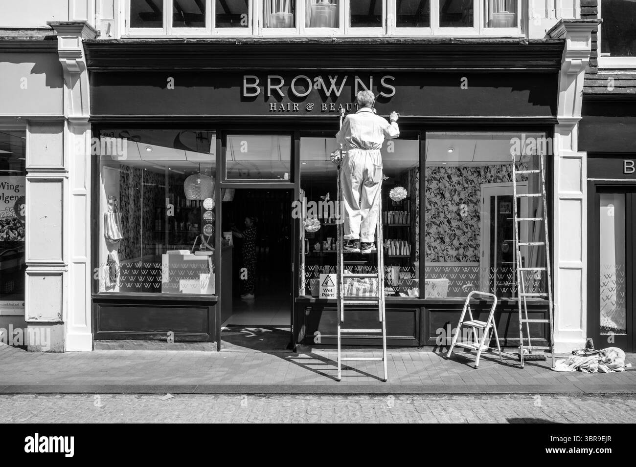 Peintre et décorateur senior peignant Une façade de magasin dans la High Street, Lewes, East Sussex, Royaume-Uni. Banque D'Images