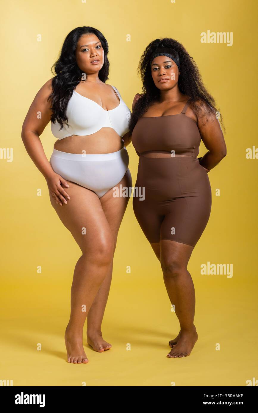 Diverses collègues féminines posant sur fond jaune portant un soutien-gorge blanc, un body marron et un bandeau Banque D'Images