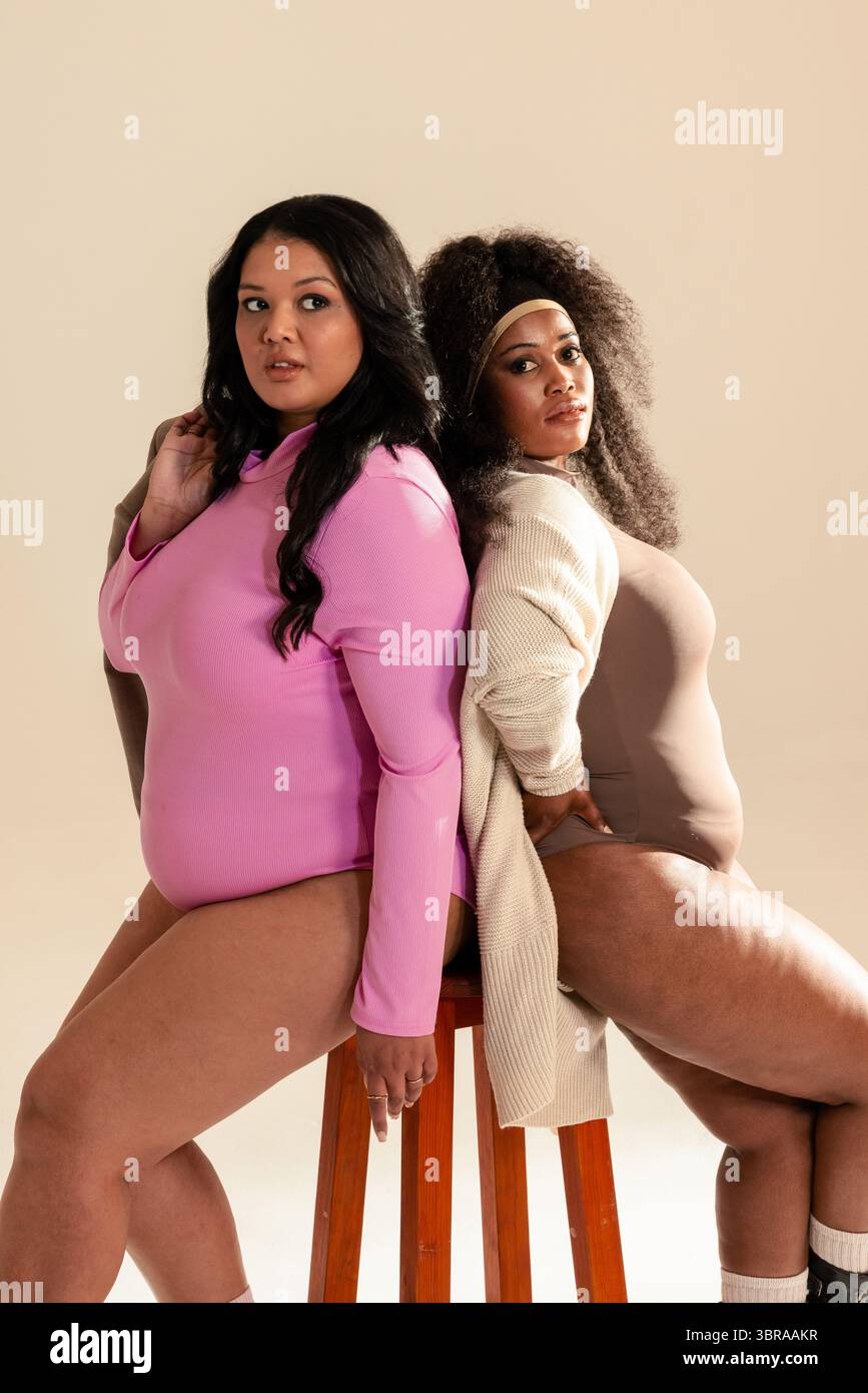 Divers modèles féminins portant un cardigan et un bandeau assis dos à dos sur un tabouret en bois dans le studio Banque D'Images