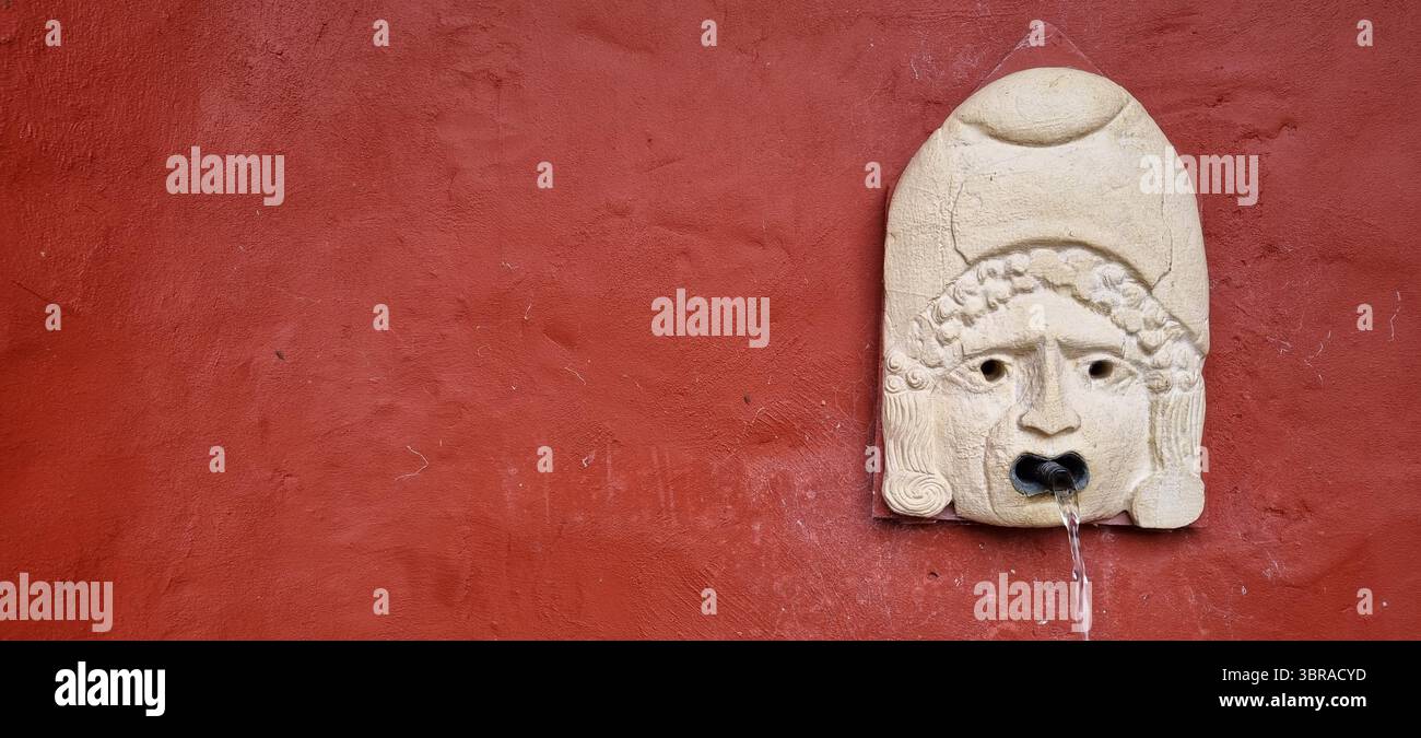 Une fontaine d'eau de style romain dans un mur de plâtre rouge. Banque D'Images