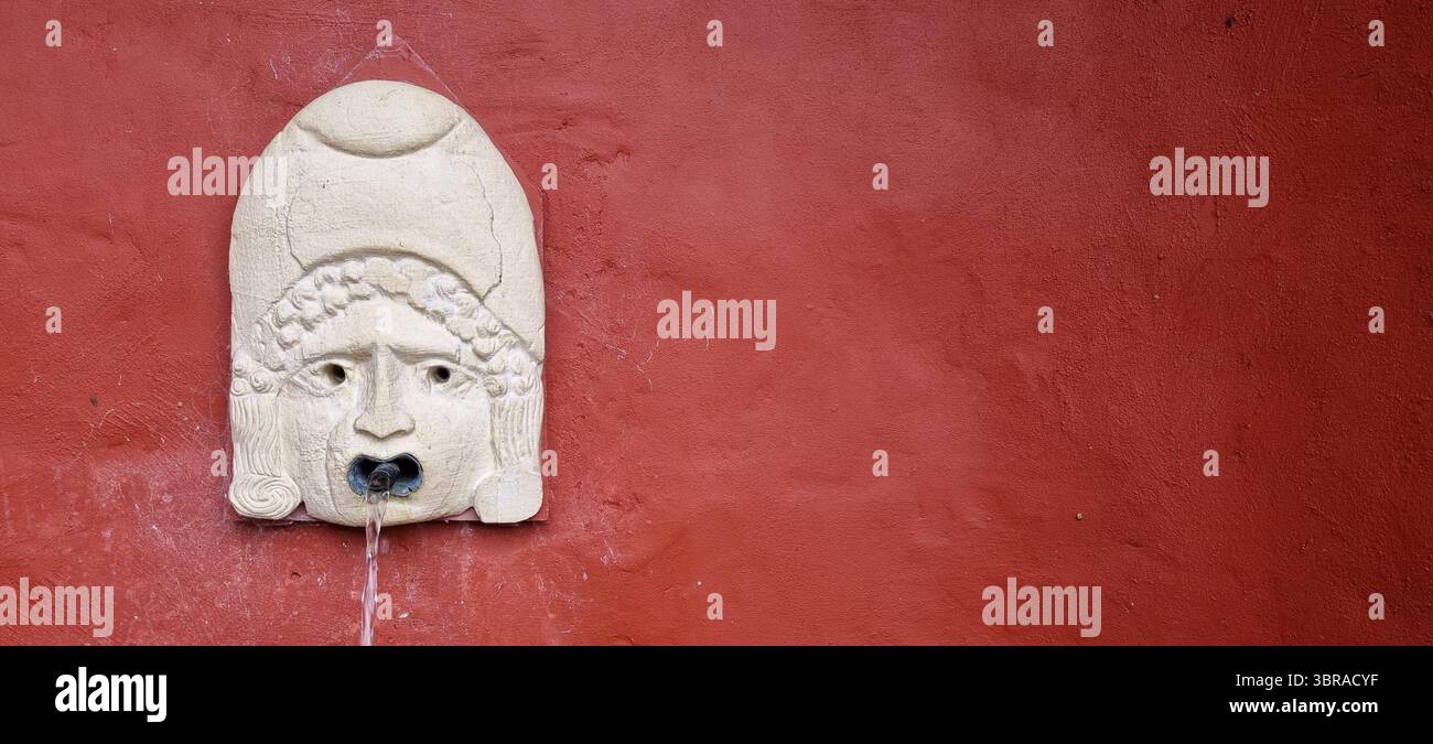 Une face en pierre sculptée avec un tuyau de fontaine d'eau dans la bouche. Banque D'Images