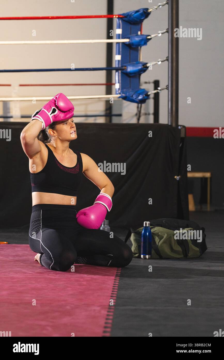 Boxer agenouillant la sueur sur le tapis rose à côté du coin de l'anneau, sac vert olive et bouteille d'eau bleue Banque D'Images
