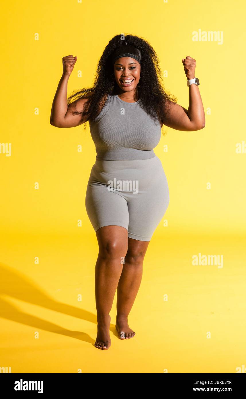 Femme afro-américaine posant avec des poings en studio portant des vêtements de sport, bandeau et smartwatch Banque D'Images