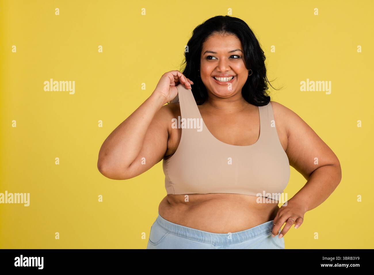 Femme grande taille tirant sur la sangle de soutien-gorge de sport et la main de repos sur les leggings en studio sur fond jaune Banque D'Images