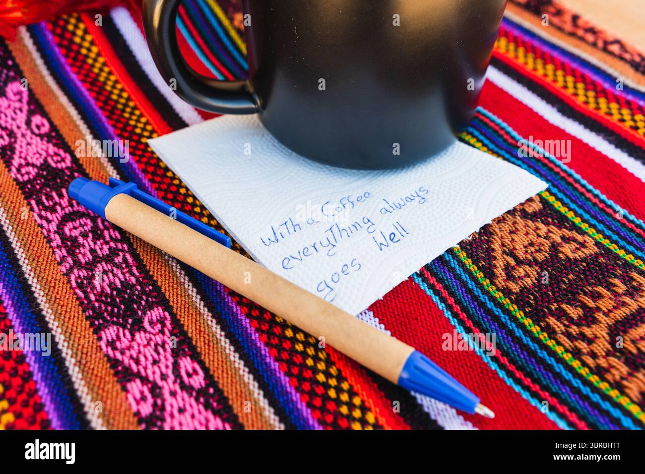 Tasse à café avec une note écrite qui dit avec une tasse de café tout va toujours bien, sur une table colorée avec du tissu inca. Banque D'Images