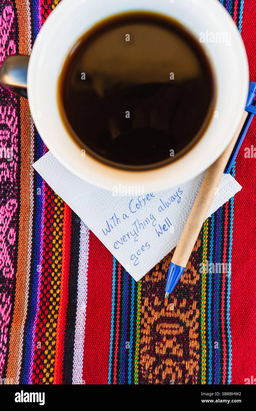 Tasse à café avec une note écrite qui dit avec une tasse de café tout va toujours bien, sur une table colorée avec du tissu inca. Banque D'Images