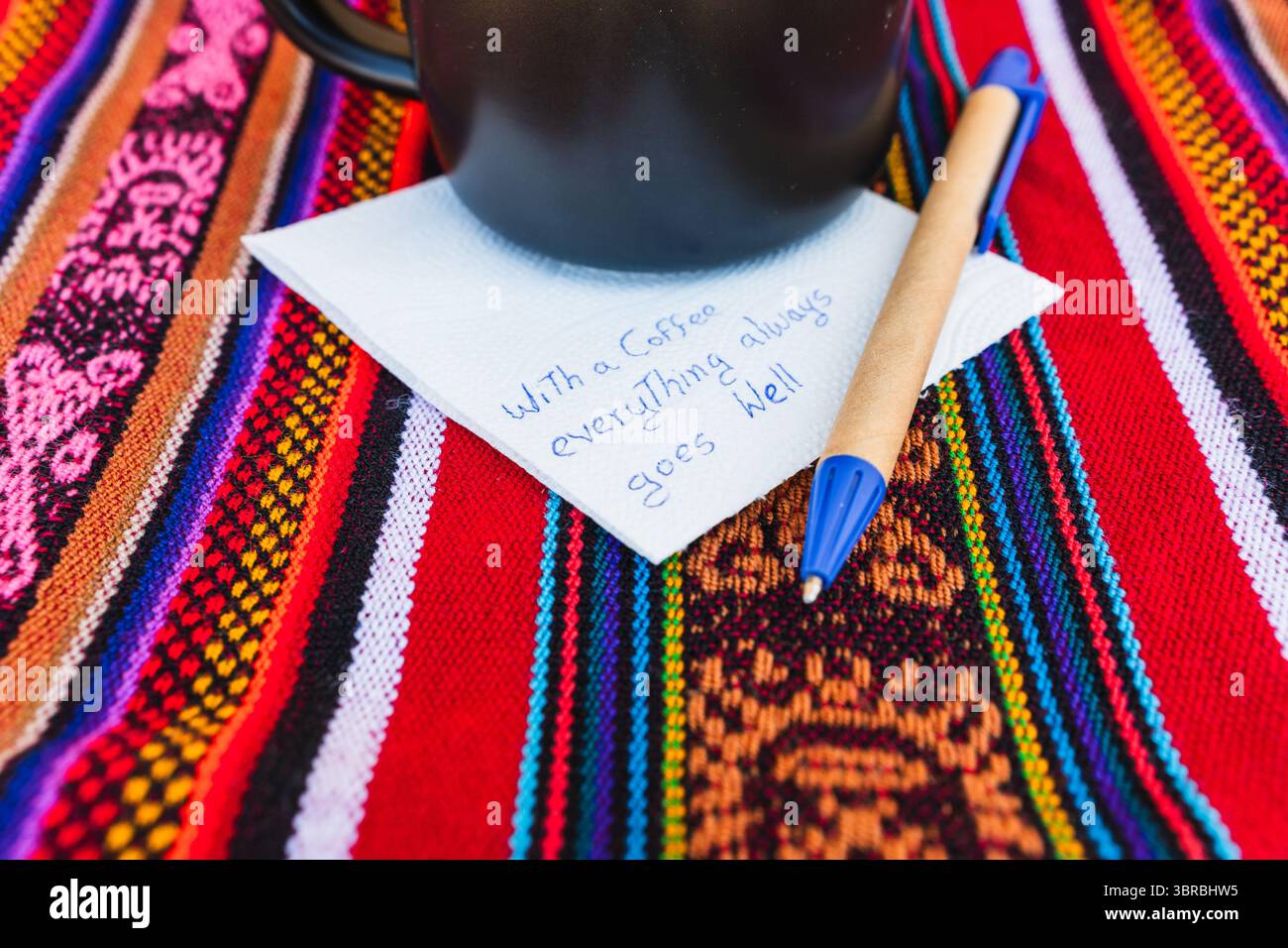 Tasse à café avec une note écrite qui dit avec une tasse de café tout va toujours bien, sur une table colorée avec du tissu inca. Banque D'Images
