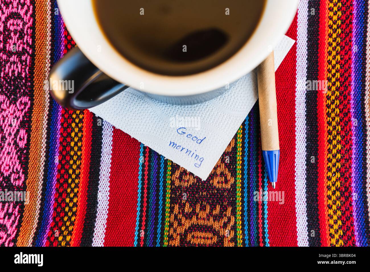 Tasse à café avec une note disant bonjour sur une table colorée avec tissage Inca. Banque D'Images