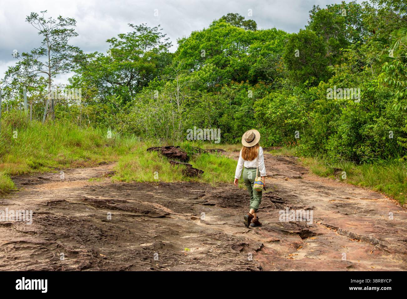 Une femme marche le long d'un chemin rocheux entouré de verdure luxuriante à Guaviare, en Colombie, parfait pour les aventures et les vacances en plein air. Banque D'Images