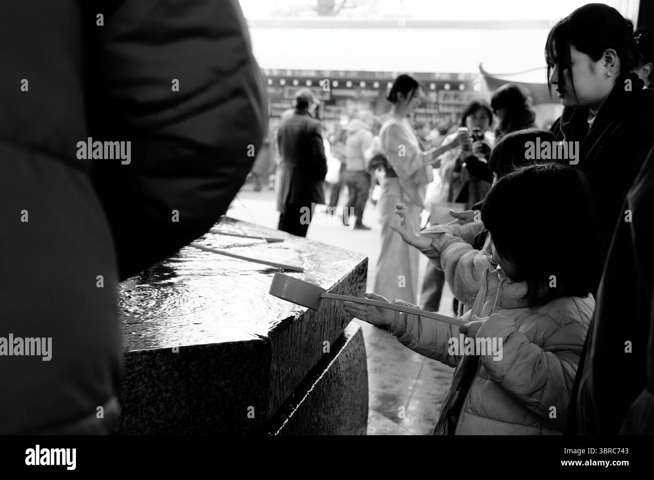Les enfants purifient les mains dans le bassin d'eau du temple Senso Ji en noir et blanc intemporel Banque D'Images