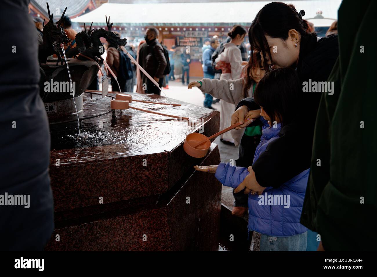 Mère guide l'enfant dans le rituel de purification dans un bassin d'eau du temple Senso Ji avec des dragons ornementaux Banque D'Images