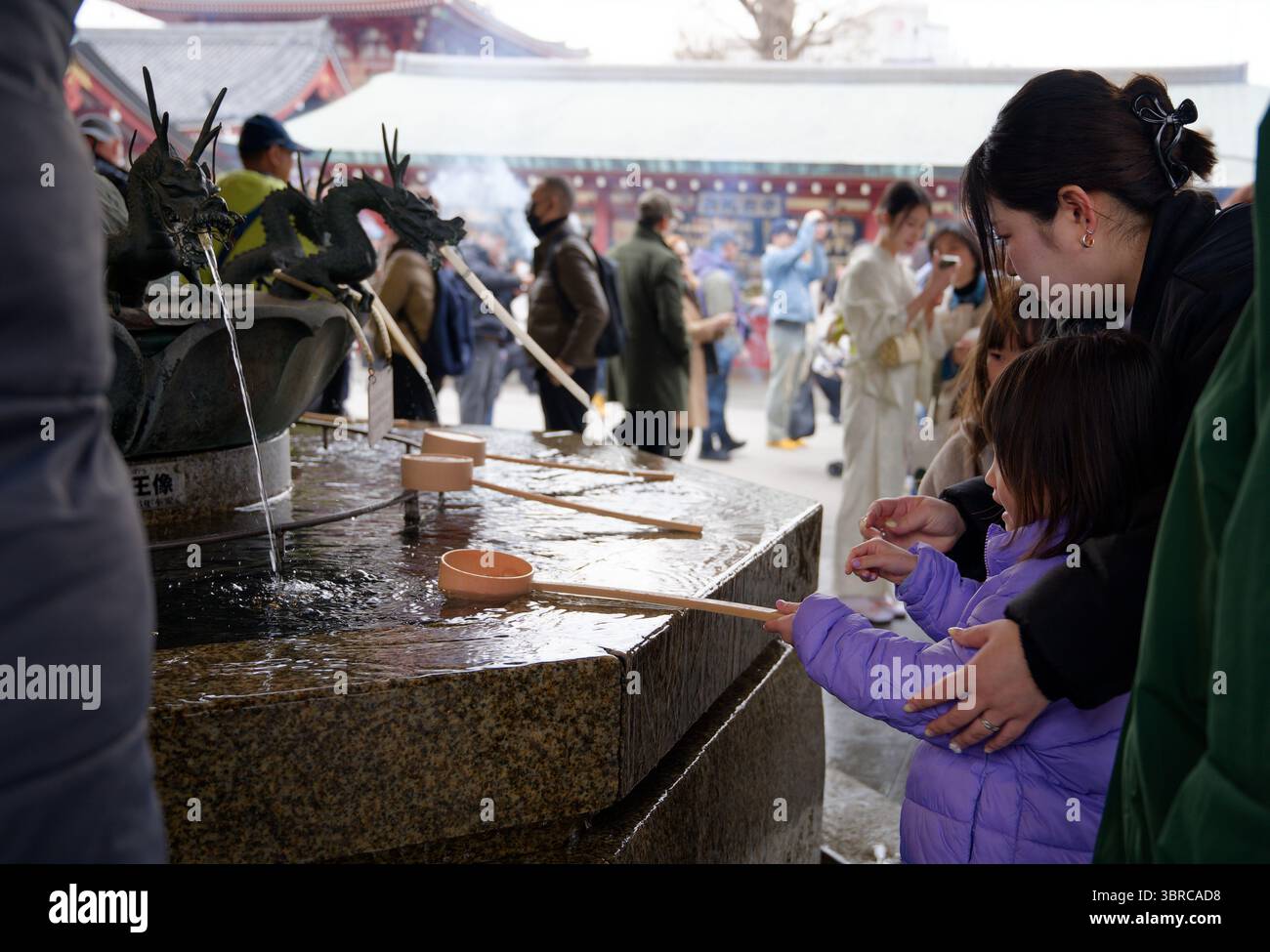 Mère guide l'enfant dans le rituel de purification au bassin d'eau du temple Senso Ji Banque D'Images