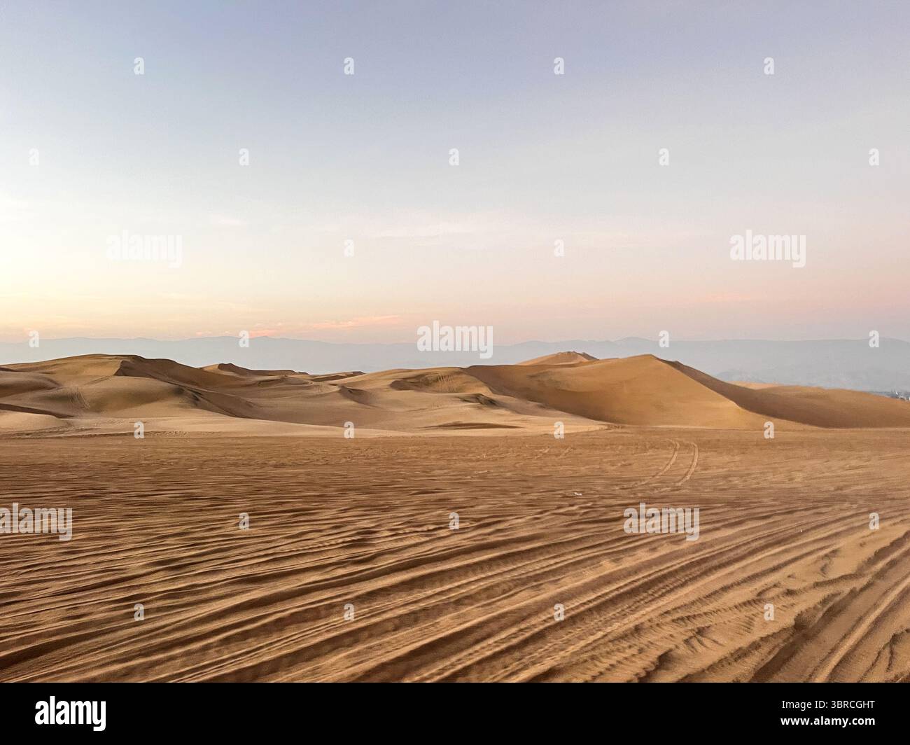 Photo du désert à l'heure du coucher du soleil au lever du soleil avec dune en arrière-plan et des traces de pneus buggy dans le sable. Excursions en buggy comme une attraction touristique Banque D'Images