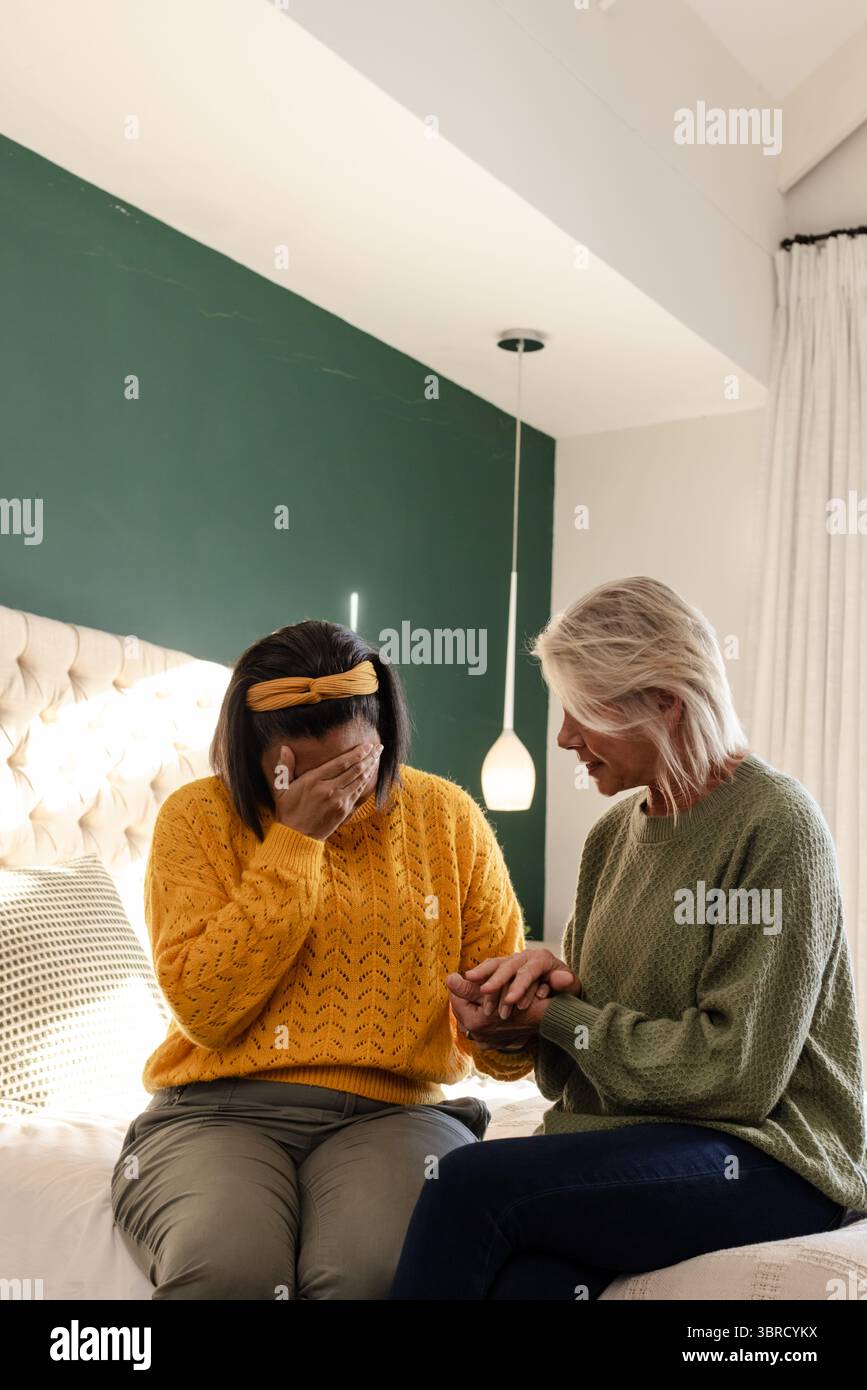 Diverses amies féminines assises sur le lit dans la chambre avec tête de lit touffetée se consolant mutuellement Banque D'Images