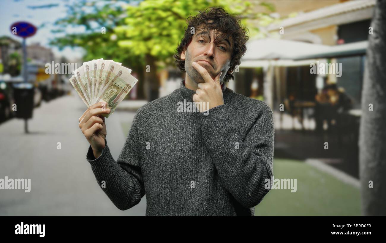 Homme hispanique tenant des roubles russes réfléchis dans une rue animée en plein air de la ville, capturant l'essence de la finance mondiale et le style de vie urbain. Banque D'Images