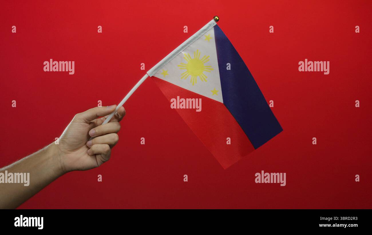 Homme tenant le drapeau philippin sur un fond rouge avec une focalisation isolée mettant en valeur le patriotisme et la fierté nationale. Banque D'Images