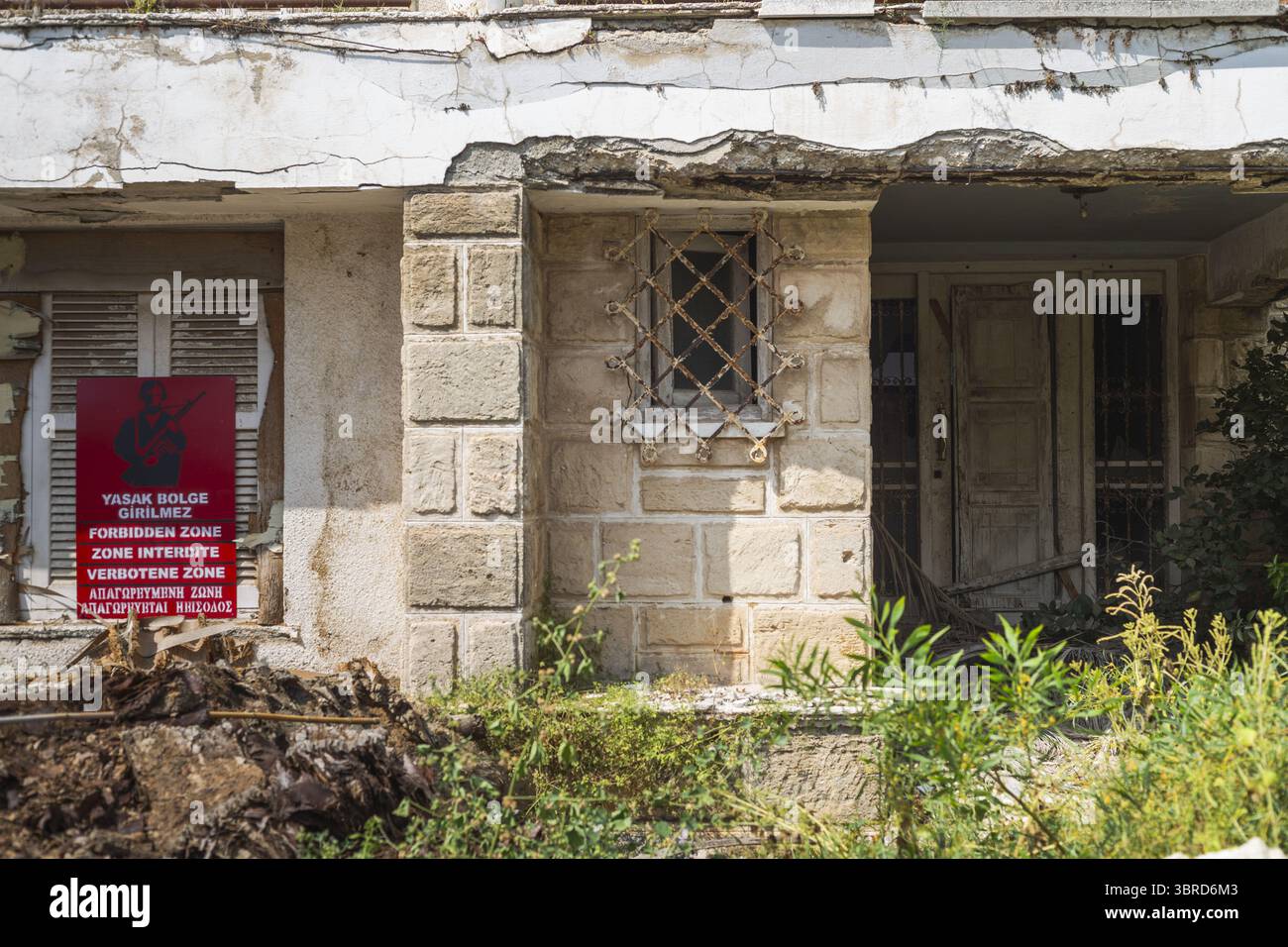 Varosha, Chypre - 25 juin 2025 : vue sur la façade en pierre altérée, un panneau de zone interdite ajoute un contraste frappant à la végétation envahie. Banque D'Images