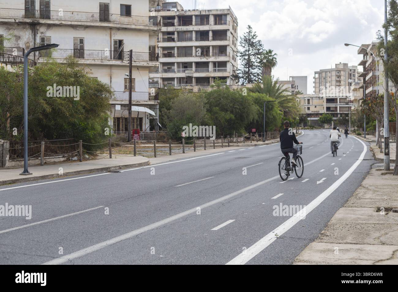 Varosha, Chypre - 25 juin 2025 : vue d'un cycliste glissant sur une route déserte bordée de bâtiments en décomposition sous un ciel silencieux. Banque D'Images