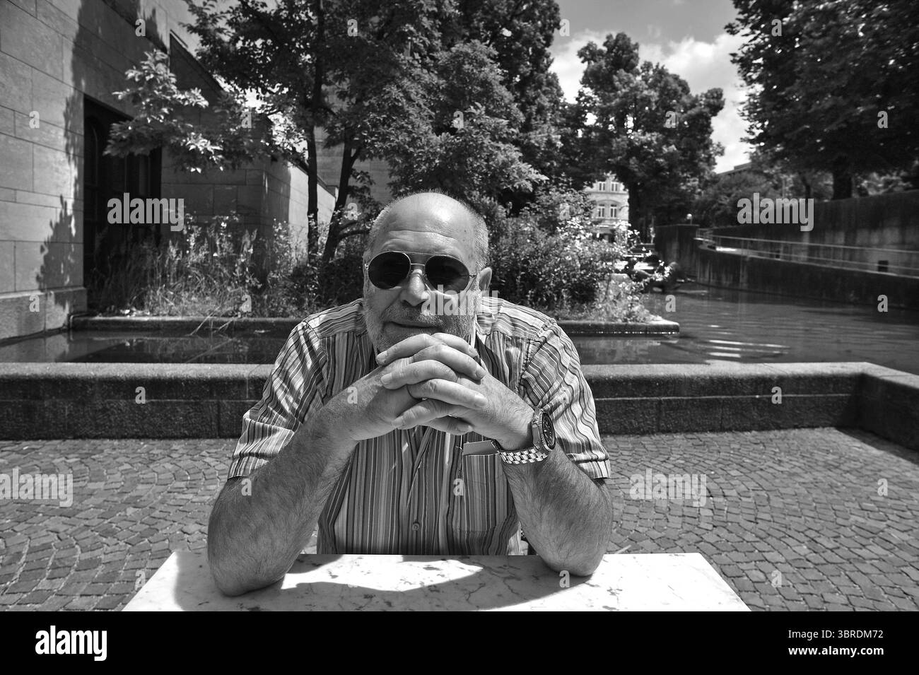 Portrait d'un homme âgé avec barbe et lunettes de soleil assis à une table, derrière lui le front de mer de la Neue Pinakothek, noir et blanc, muni Banque D'Images