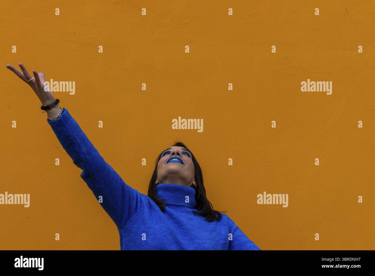 Portrait d'une femme heureuse avec le bras levé et regardant vers le haut vêtue de bleu sur fond jaune Banque D'Images