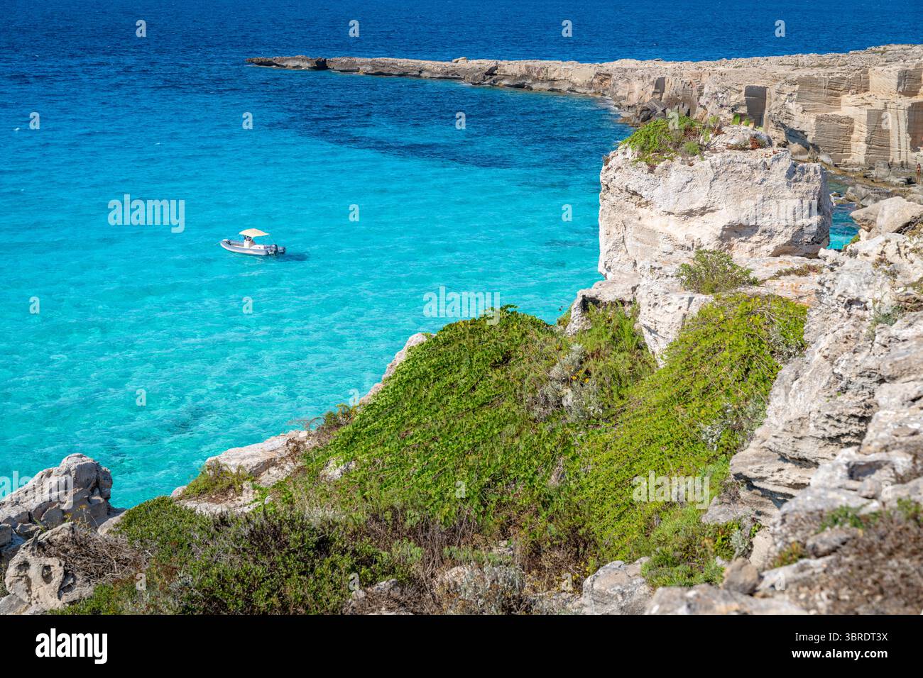 Le bateau repose dans les eaux turquoises au large de la côte rocheuse, profitant du soleil méditerranéen. Favignana Banque D'Images