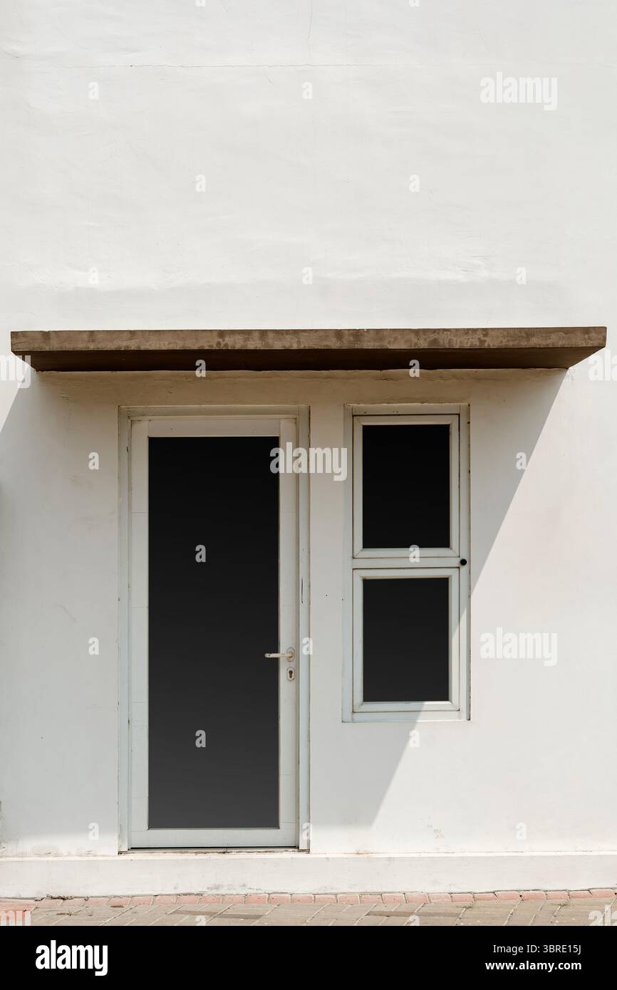 Un mur blanc minimaliste d'une maison avec une porte en verre foncé, une petite fenêtre et un auvent en béton. Propre, simple détail architectural et des Banque D'Images