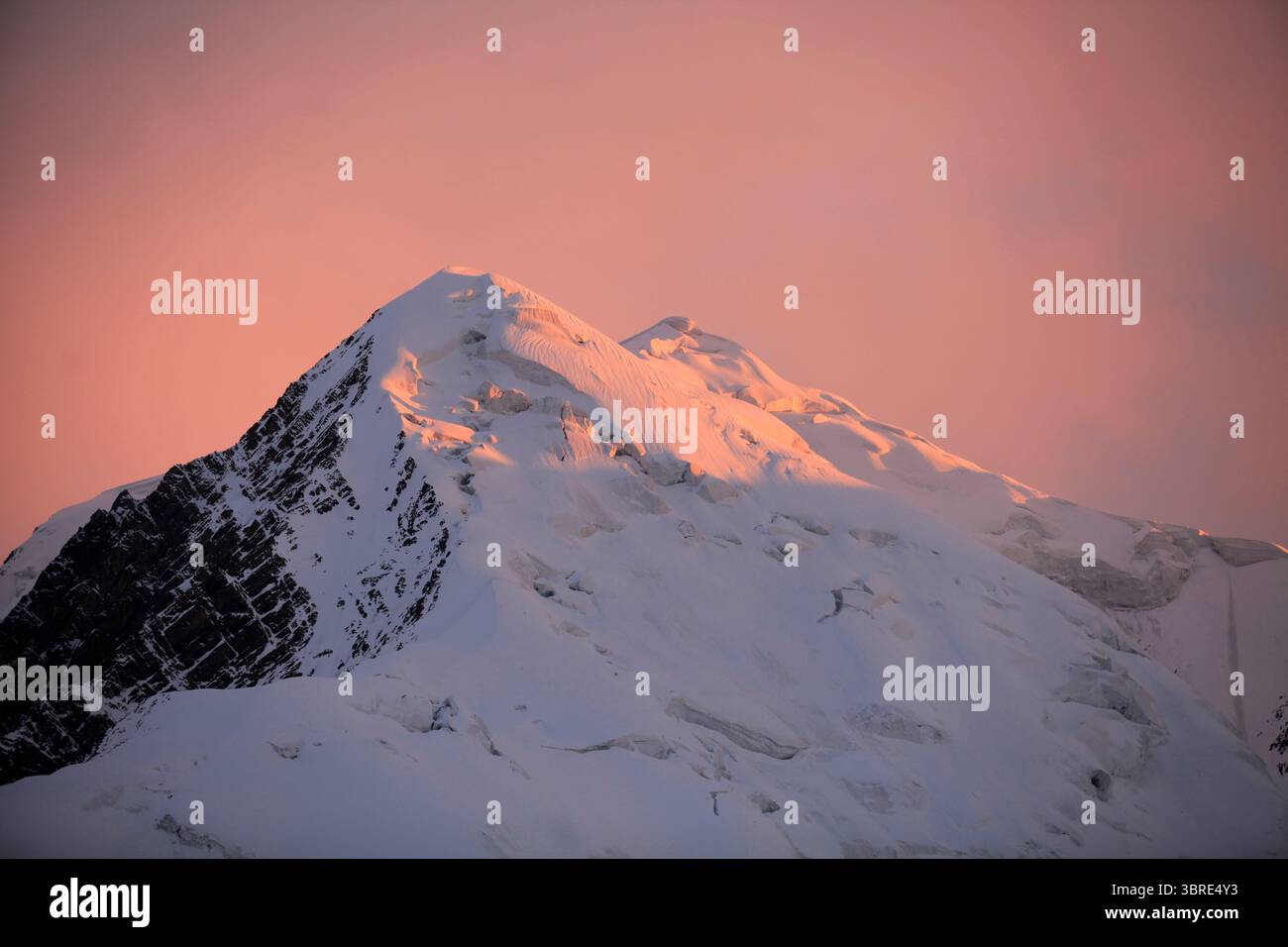 Pamir Peak recouvert de glace brille rose dans la lumière du coucher du soleil. Une scène alpine onirique avec une montagne et un ciel teintés de rose, vue sur la route alpine vers Lénine Peak. Banque D'Images