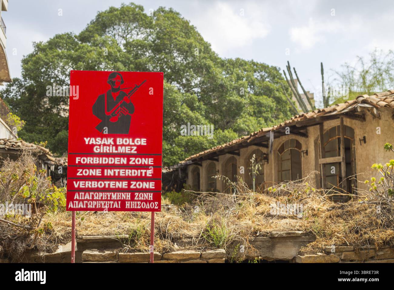 Vue d'un panneau rouge de zone interdite avec une silhouette de soldat au milieu de bâtiments en ruine et de feuillage envahi par la végétation, Varosha, Famagouste, Chypre. Banque D'Images