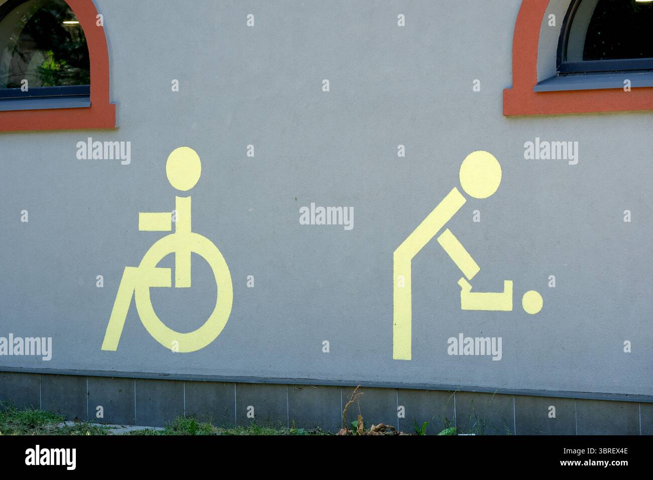 Des symboles jaune vif sur un mur gris représentent l'accès en fauteuil roulant et la prestation de soins. Banque D'Images