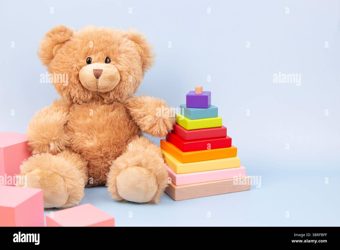 Fond de jouets pour enfants. Ours en peluche, pyramide empilable et cubes roses sur fond bleu. Jouets éducatifs Montessori pour enfants. Vue de face Banque D'Images