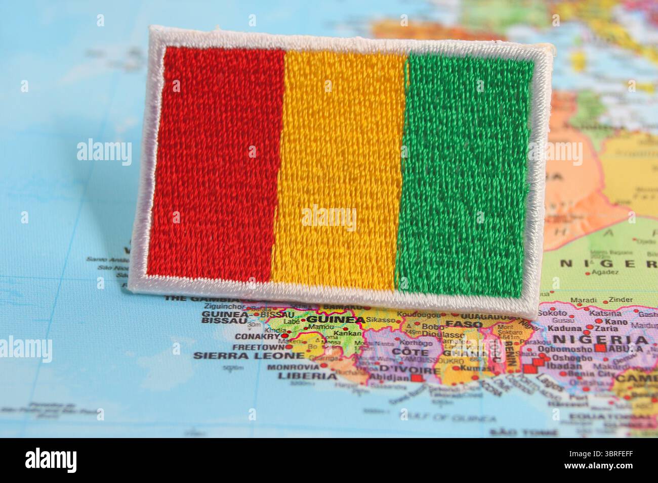 Drapeau de Guinée brodé écologique placé sur la carte du monde à son emplacement, symbolisant le voyage vert, la fierté culturelle et la sensibilisation à l'environnement. Banque D'Images