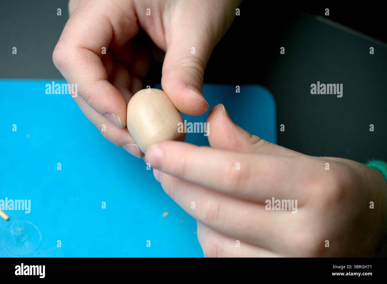 Les mains façonnent soigneusement un petit objet en argile sur une surface artisanale bleue. Banque D'Images