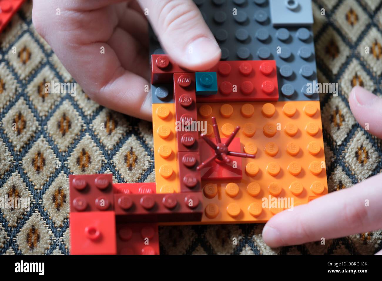 Mains assemblant soigneusement une structure Lego vibrante sur une surface à motifs. Banque D'Images