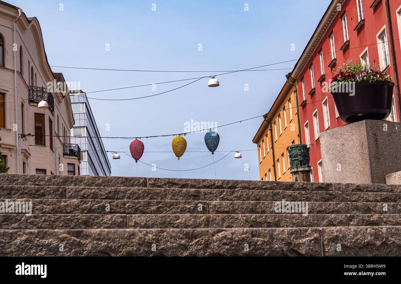 Sodertalje, Suède - 6 juin 2025 : une scène de rue pittoresque avec des lanternes suspendues colorées au-dessus d'un escalier en pierre, flanqué d'un bâtiment vibrant Banque D'Images