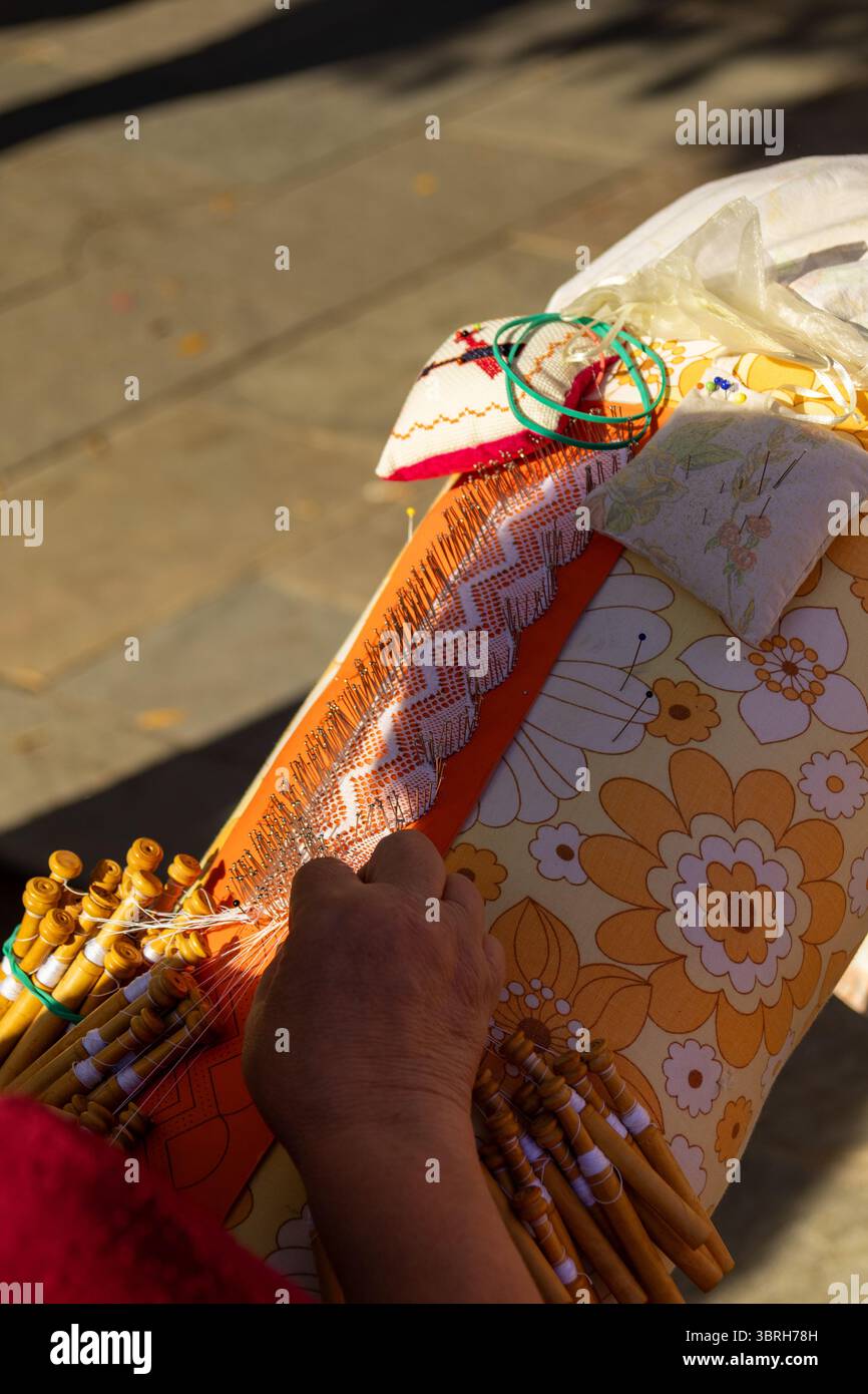 Gros plan des mains travaillant sur la dentelle de bobine, mettant en valeur l'artisanat traditionnel et le processus complexe de création de textiles délicats Banque D'Images