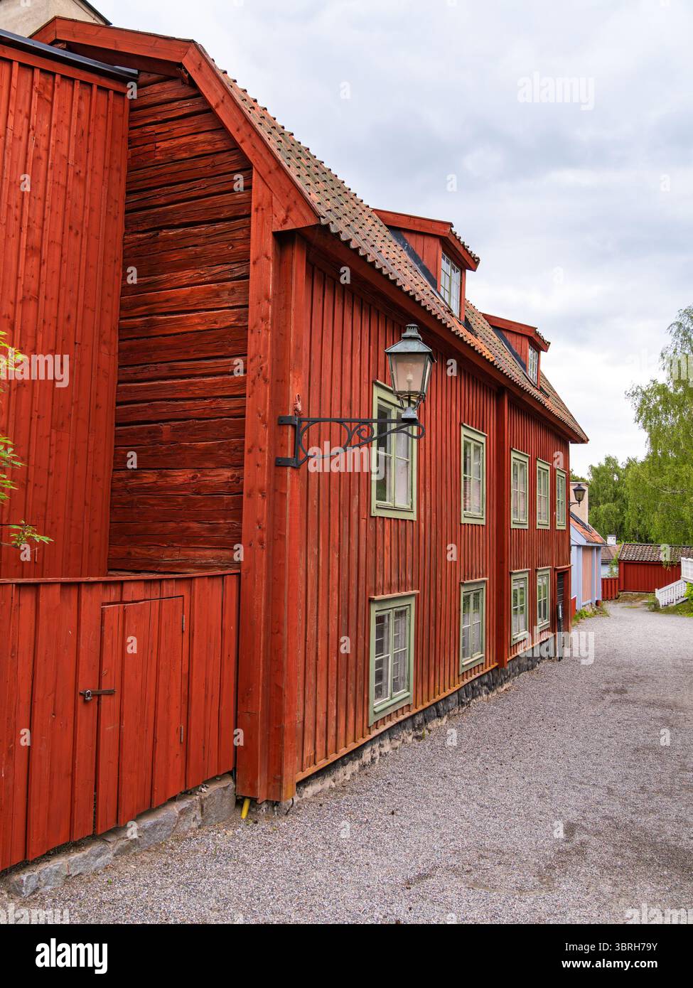 Sodertalje, Suède - 6 juin 2025 : une charmante maison en bois rouge avec un toit en pente et des cadres de fenêtres verts. Le bâtiment dispose d'une lanterne et est surr Banque D'Images