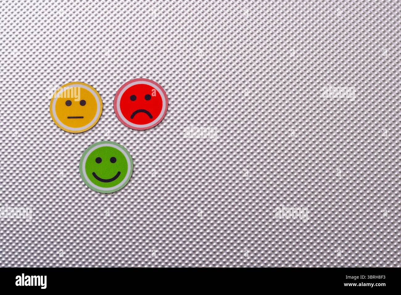 Trois visages emoji ronds en rouge, jaune et vert représentant des émotions tristes, neutres et heureuses sur un fond texturé métallique, symbolisant Banque D'Images