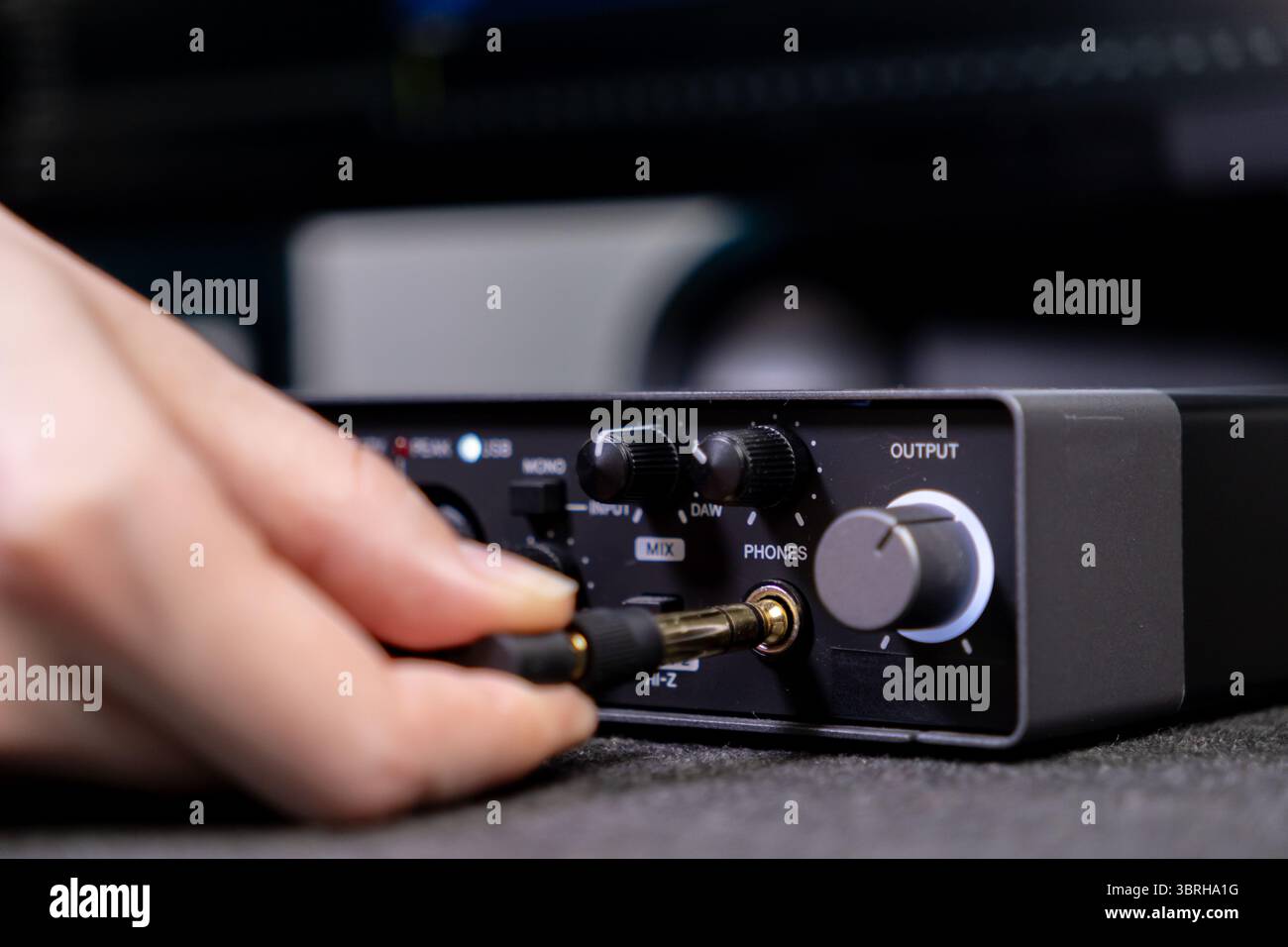 Gros plan d'une main connectant une prise audio dorée à une carte son professionnelle, soulignant le processus complexe de création de musique ou d'enregistrement aud Banque D'Images