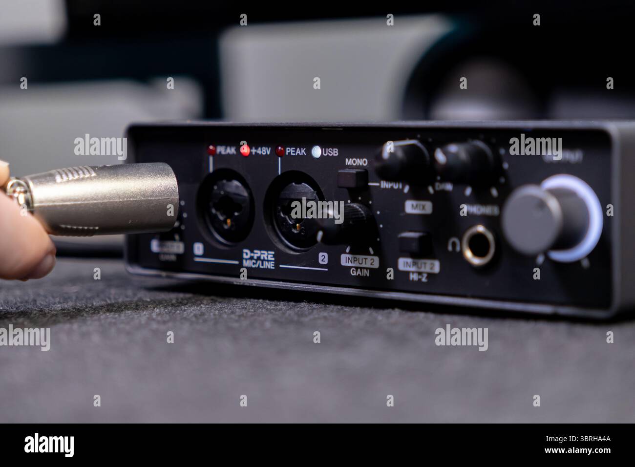 Vue rapprochée d'une main connectant un câble XLR à une interface audio, mettant en évidence l'entrée, le gain, le mixage, les téléphones, et des commandes de sortie pour sou professionnel Banque D'Images