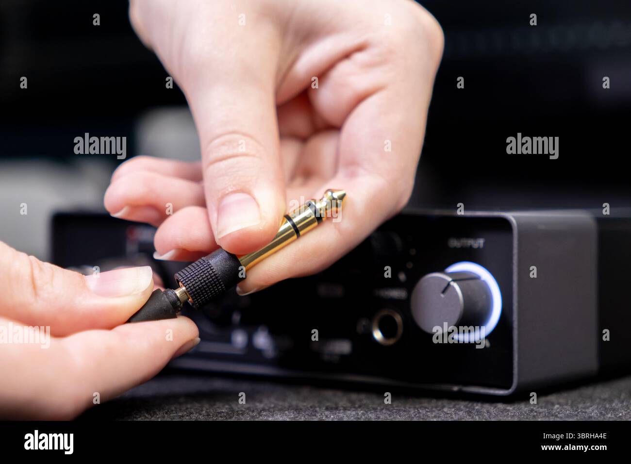 Photo détaillée d'une main connectant une prise audio dorée au port DE SORTIE D'un périphérique Dark Sound, montrant la configuration pour l'enregistrement de musique et l'aud professionnel Banque D'Images