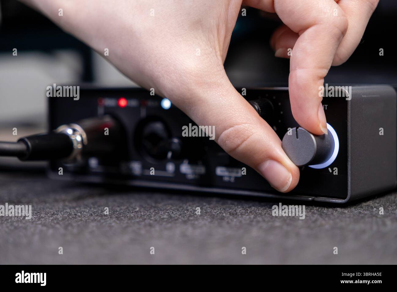 Gros plan d'une main tournant un cadran sur une carte son noire élégante, indiquant un contrôle audio précis pour l'enregistrement, le podcasting et le produit de contenu numérique Banque D'Images